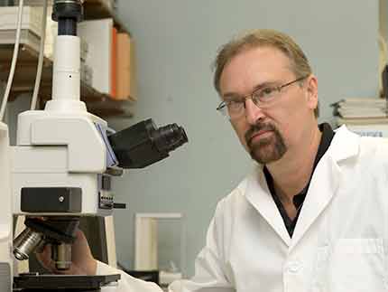 Dr. Larry Sanford sits next to a microscope in the lab.