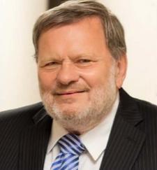 John Morley wearing black suit, white shirt, blue tie