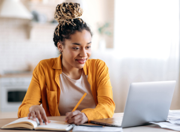 Female student smiling at her laptop while taking notes.