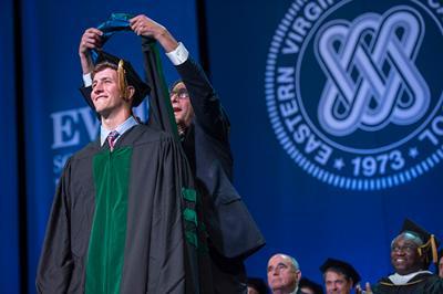 A man dons a hood on new doctoral graduate in 2019.