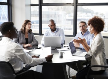 A group of diverse young professionals meet around a conference room table 