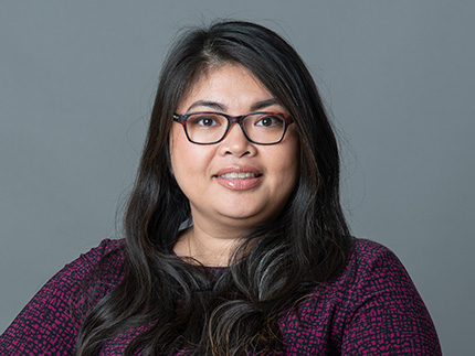 Woman with dark hair and glasses smiles at the camera