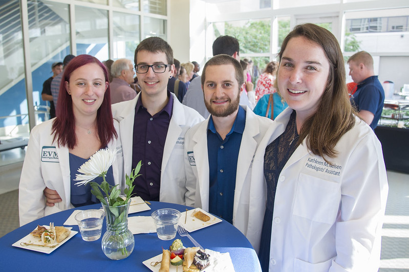 A group of Physicians' Assistant graduates wearing white coats smile during a reception