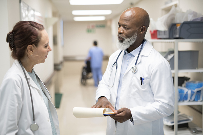 Two doctors discuss a chart in a hospital hallway.