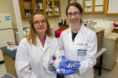 Two biorepository staff face the camera holding out their hands holding specimens