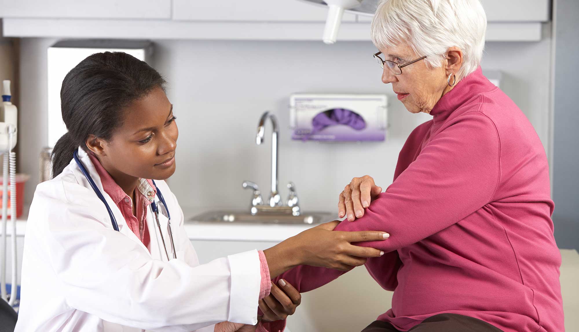 A physician examines a patient's elbow.