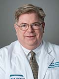 Mark Cotterell, MD, smiles at the camera wearing his white coat.